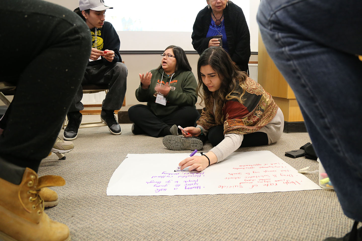Groupe de jeunes qui discutent entre eux et qui écrivent sur une grande feuille de papier.