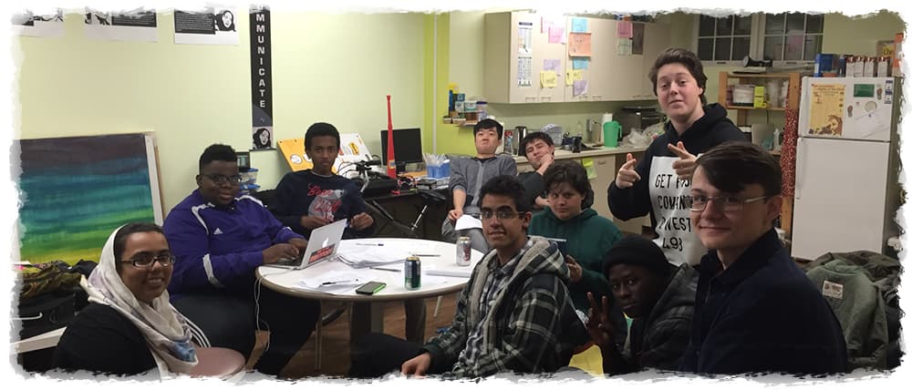 Group of young people gathered in a community room, engaging in a collaborative activity and smiling at the camera.
